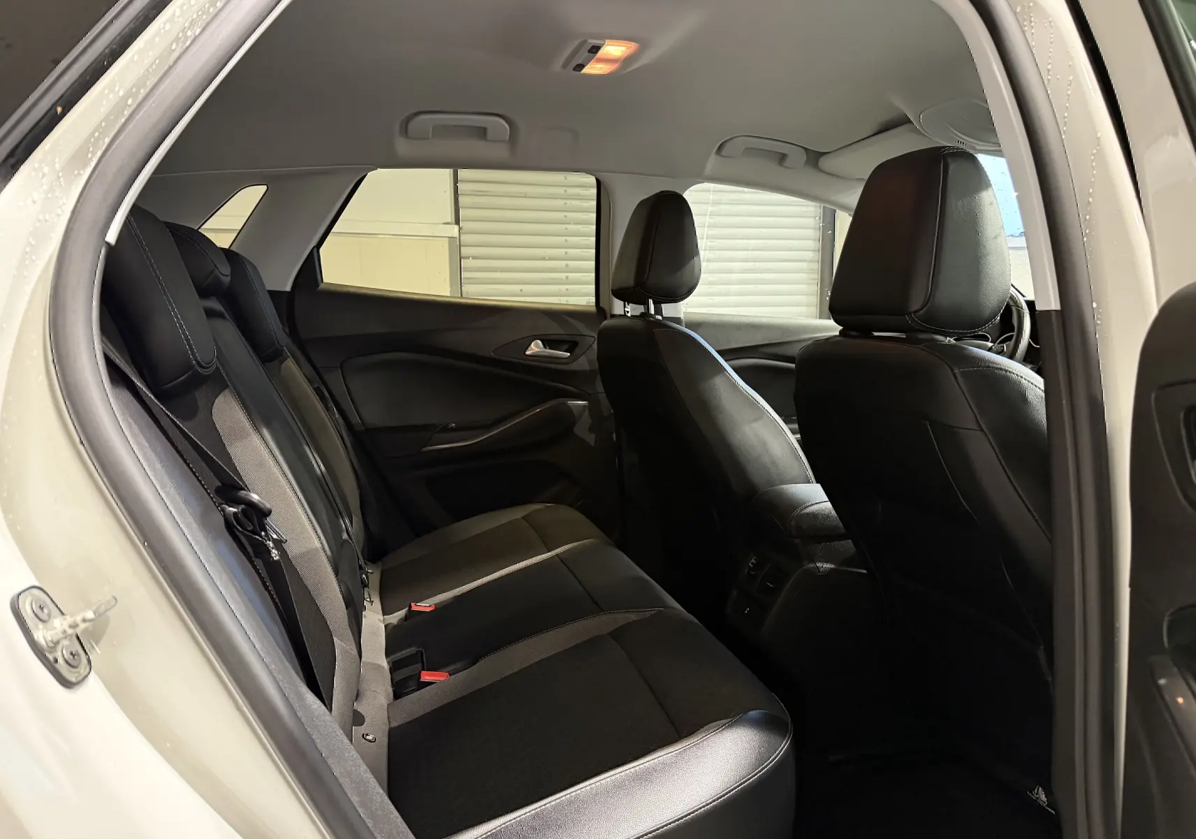 Vue intérieure arrière côté gauche de l’Opel Grandland X blanc, montrant les sièges arrière en cuir noir et tissu gris.