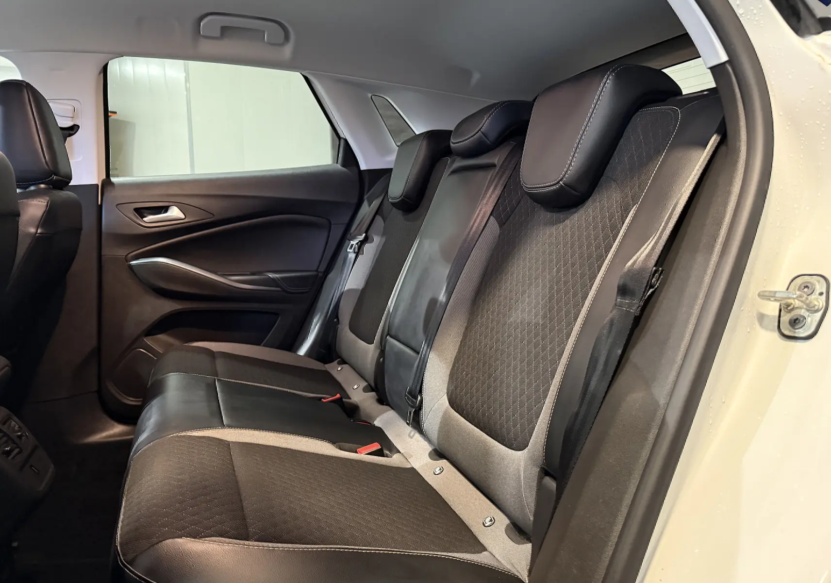 Vue intérieure côté droit des sièges arrière noirs et gris du Opel Grandland X blanc, montrant les appuie-têtes et la portière ouverte.