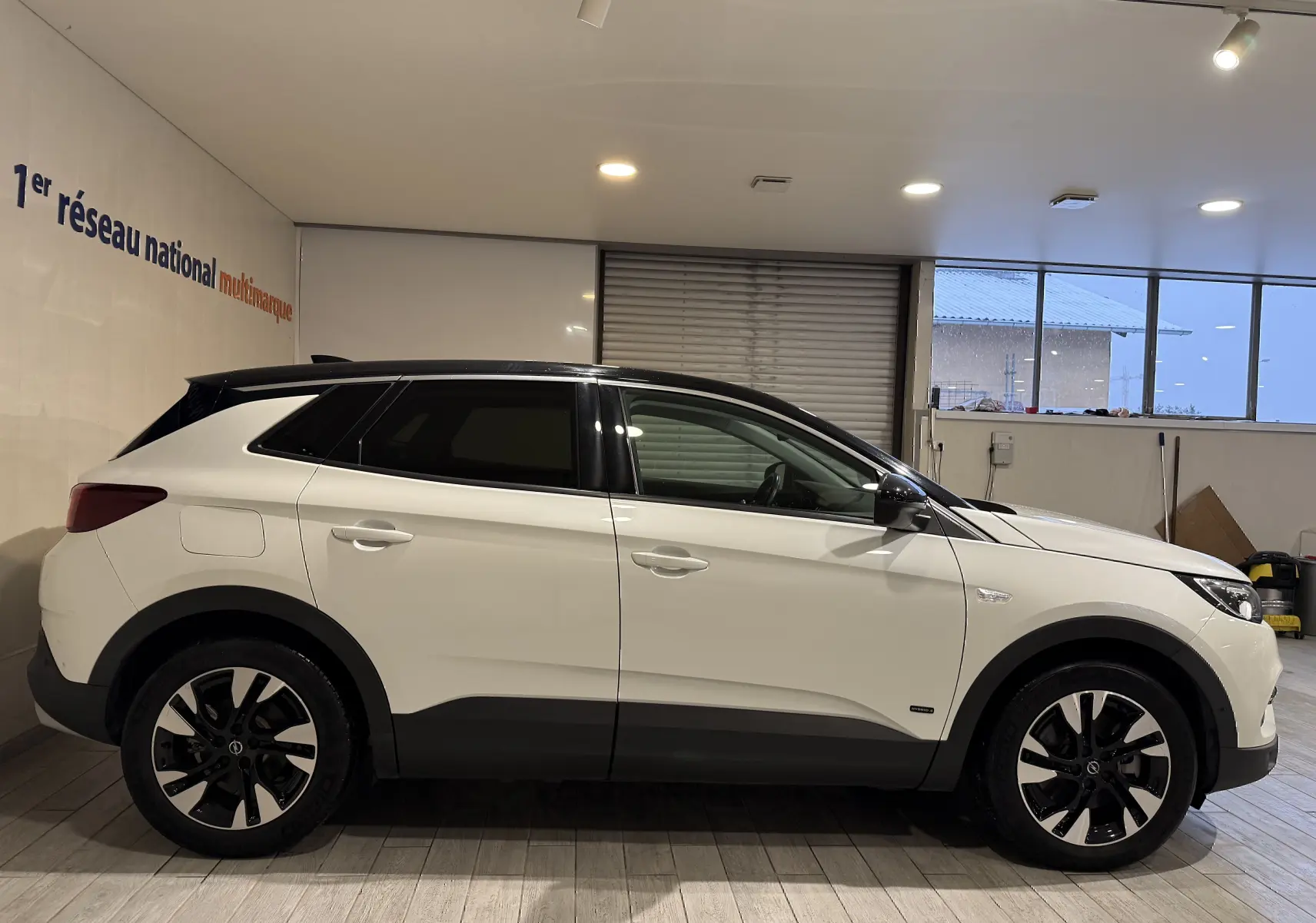 Opel Grandland X hybride rechargeable blanc en profil droit, toit noir et jantes bicolores en intérieur showroom.