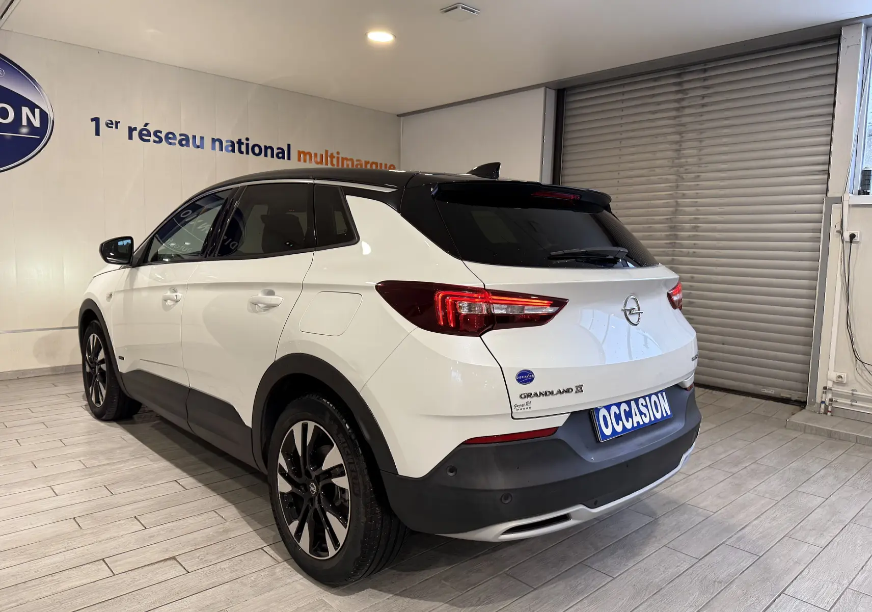 Vue 3/4 arrière droite d’un Opel Grandland X blanc hybride rechargeable, toit noir, en intérieur showroom.