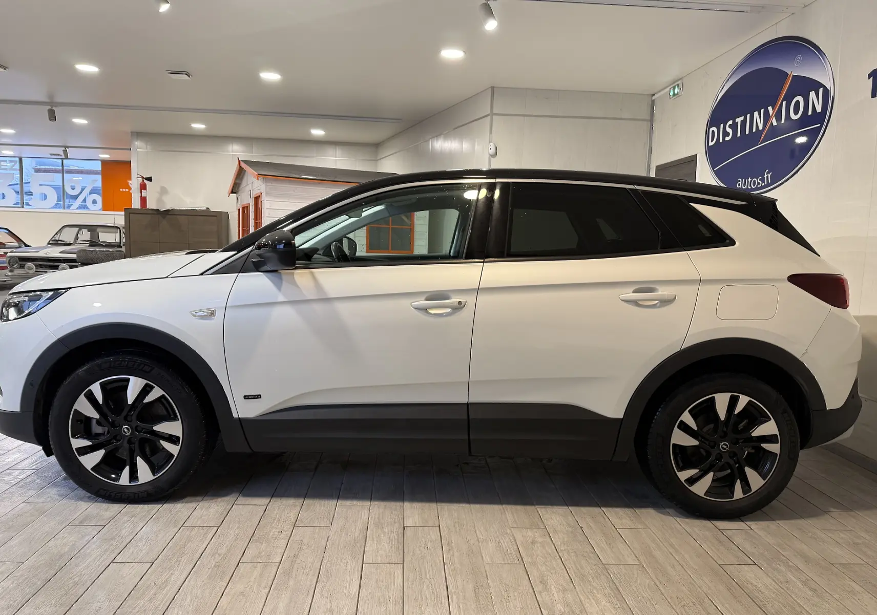 Vue de profil côté gauche d'un Opel Grandland X blanc hybride rechargeable avec jantes noires et toit noir en intérieur showroom.