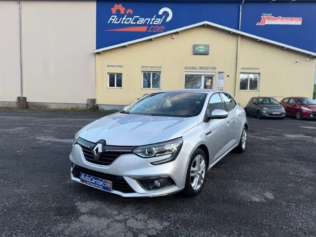 Renault Mégane gris alu vue 3/4 avant droit, avec phares LED et jantes alliage, stationnée devant un garage AutoCantal.