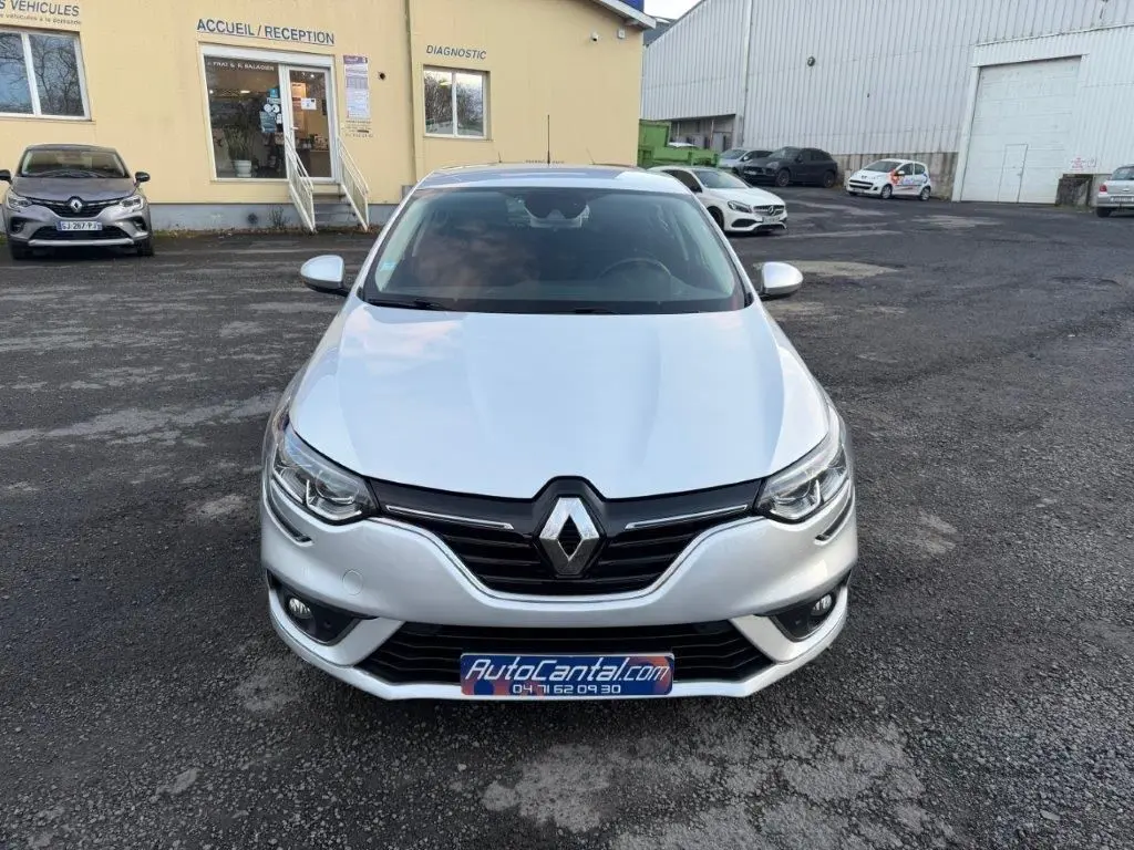 Vue avant d'une Renault Mégane gris alu 2019, avec calandre noire et phares LED visibles, stationnée devant un bâtiment.