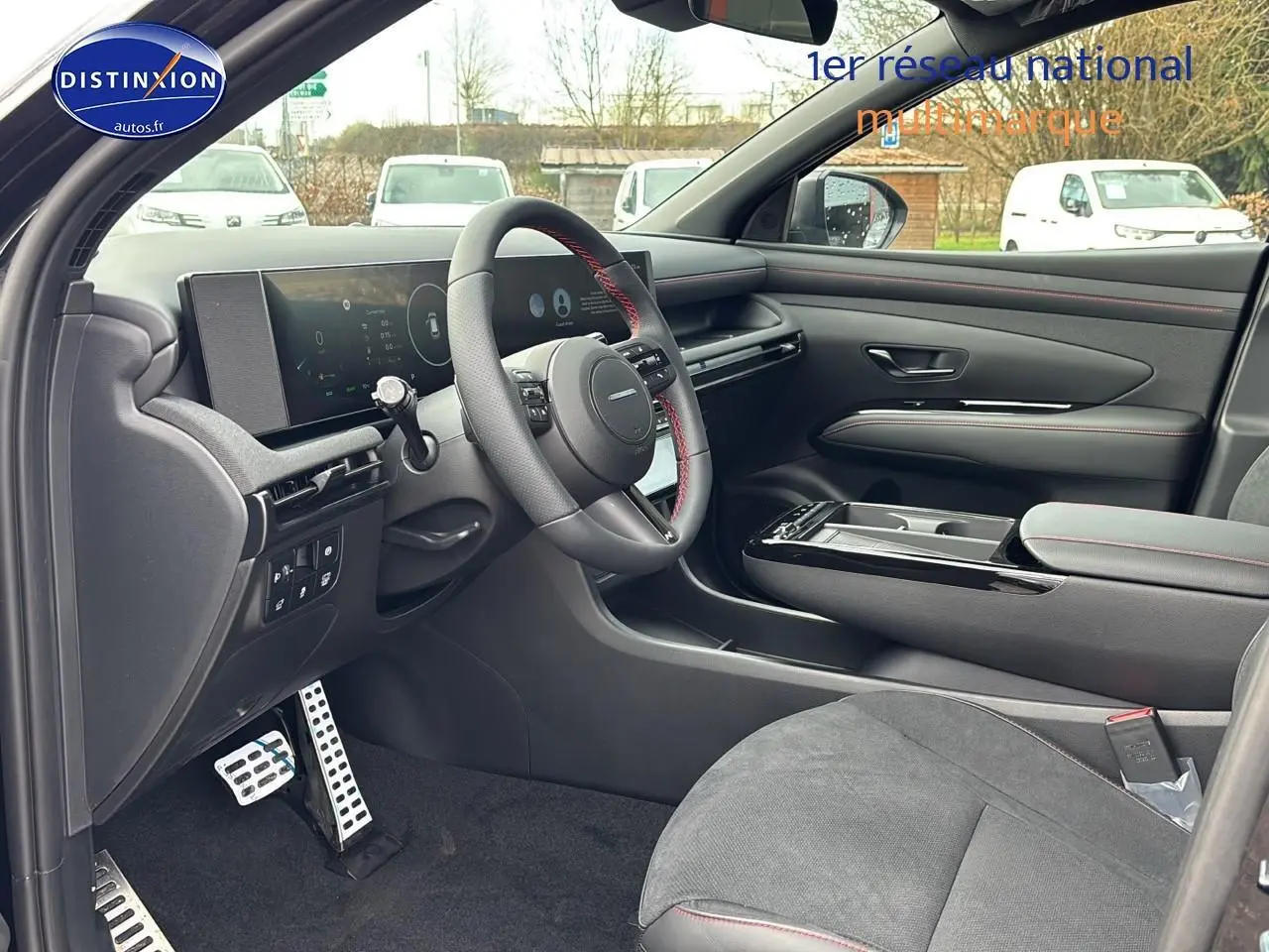 Vue intérieure côté conducteur du Hyundai Tucson 2026 noir, volant cuir avec surpiqûres rouges et tableau de bord numérique.