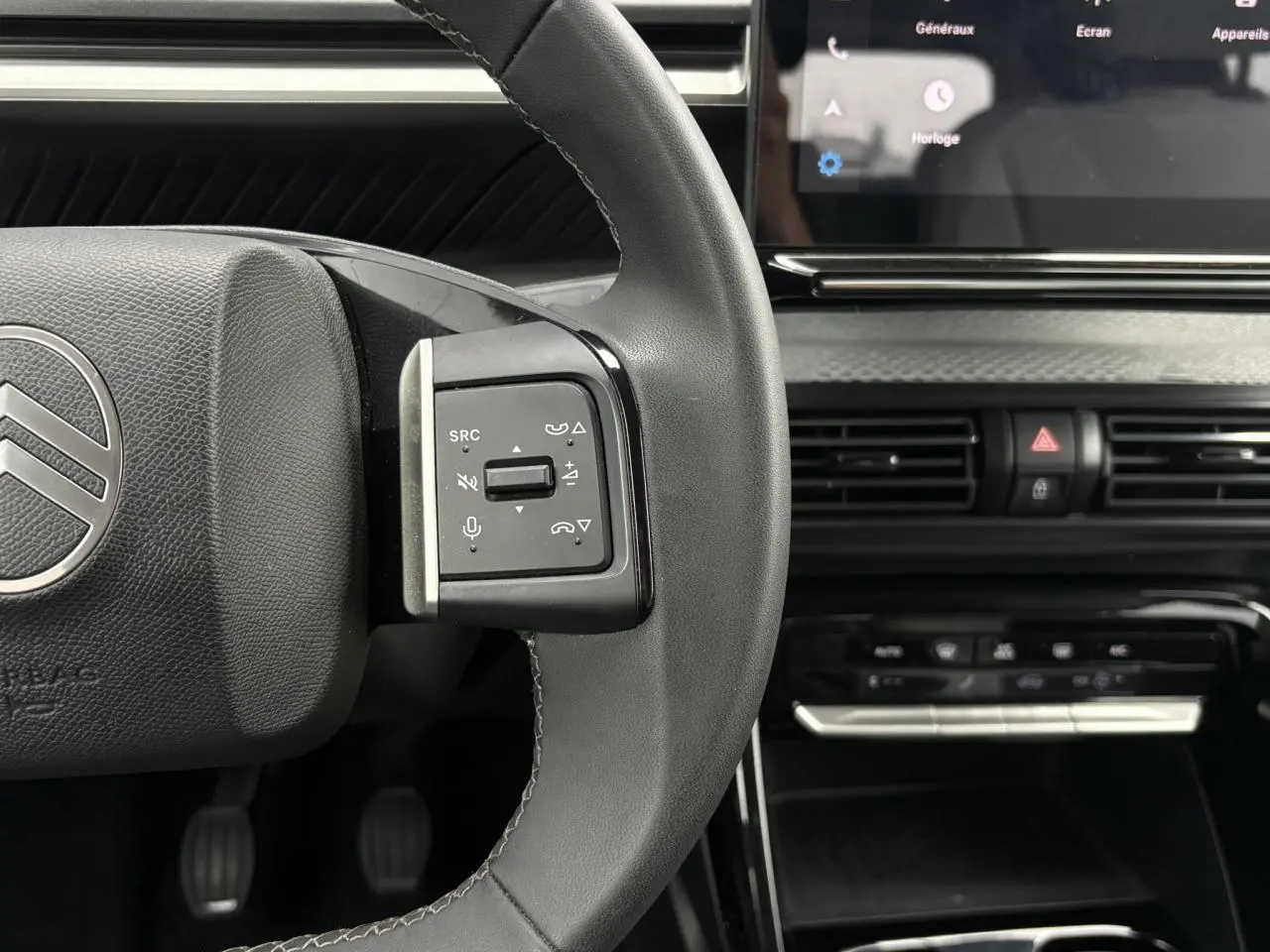 Gros plan sur le volant noir de la Citroën C3 2025 avec commandes audio et écran tactile en arrière-plan.