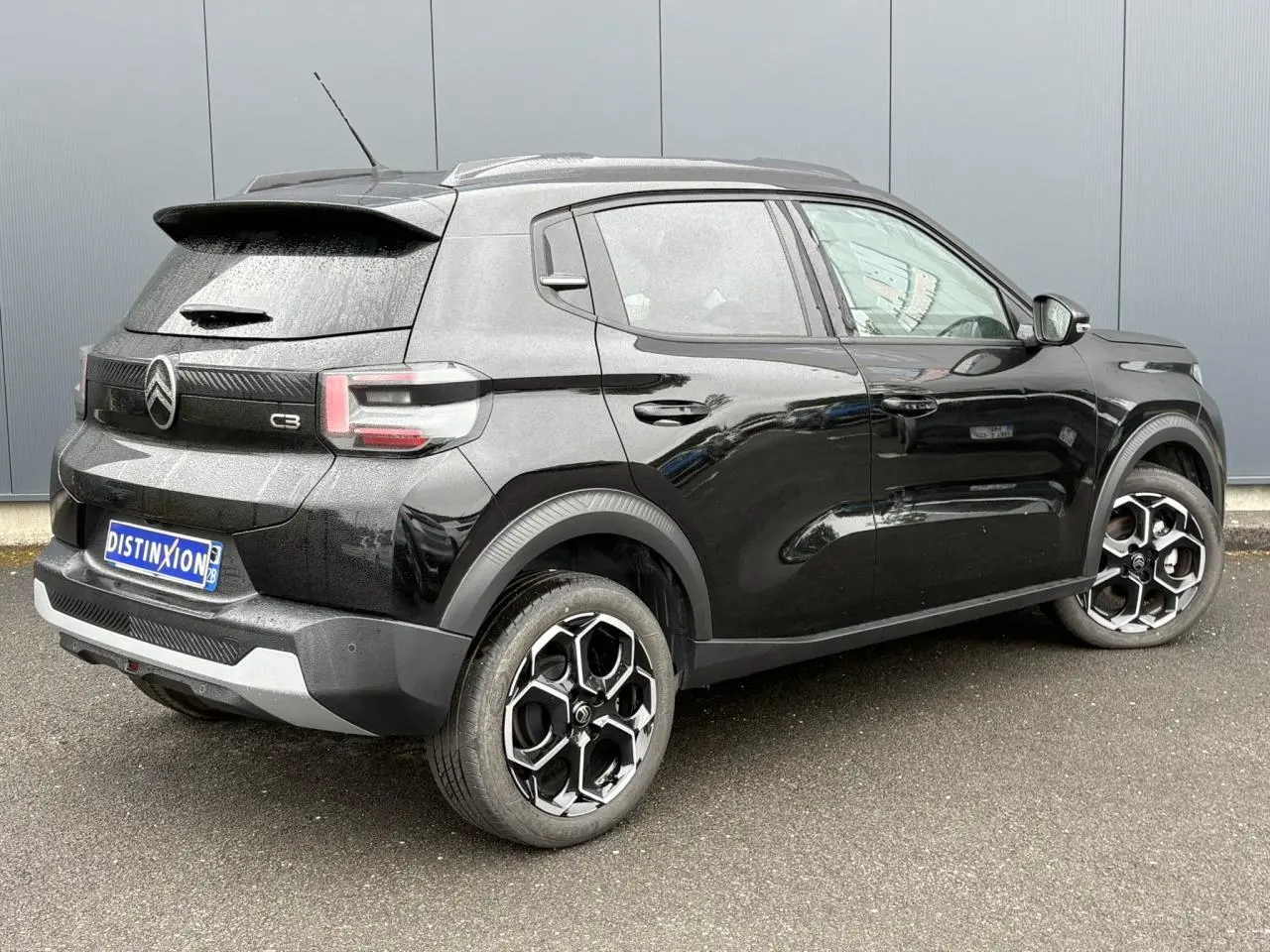 Vue 3/4 arrière droite d'une Citroën C3 Turbo 100 Max noire Perla avec jantes alliage 17 pouces et barres de toit noires.