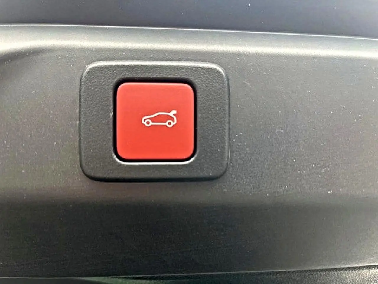 Bouton rouge d'ouverture électrique du coffre sur un Peugeot 3008 gris titane, vue en gros plan intérieur.