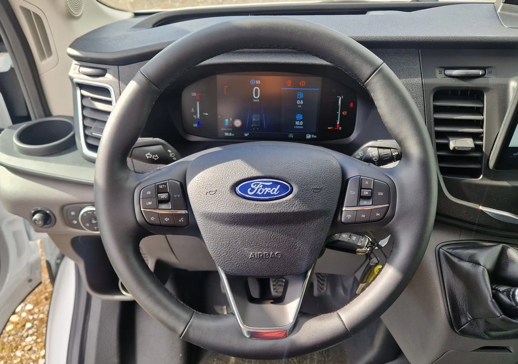 Vue intérieure centrée sur le volant noir du Ford Transit Chassis Cabine 2026 avec tableau de bord numérique allumé.