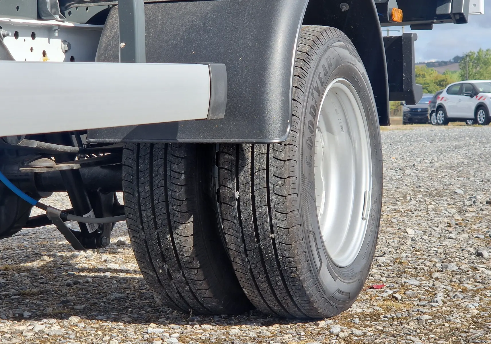 Gros plan sur les roues jumelées arrière du Ford Transit Châssis Cabine blanc, avec benne acier et coffre visible en arrière-plan.