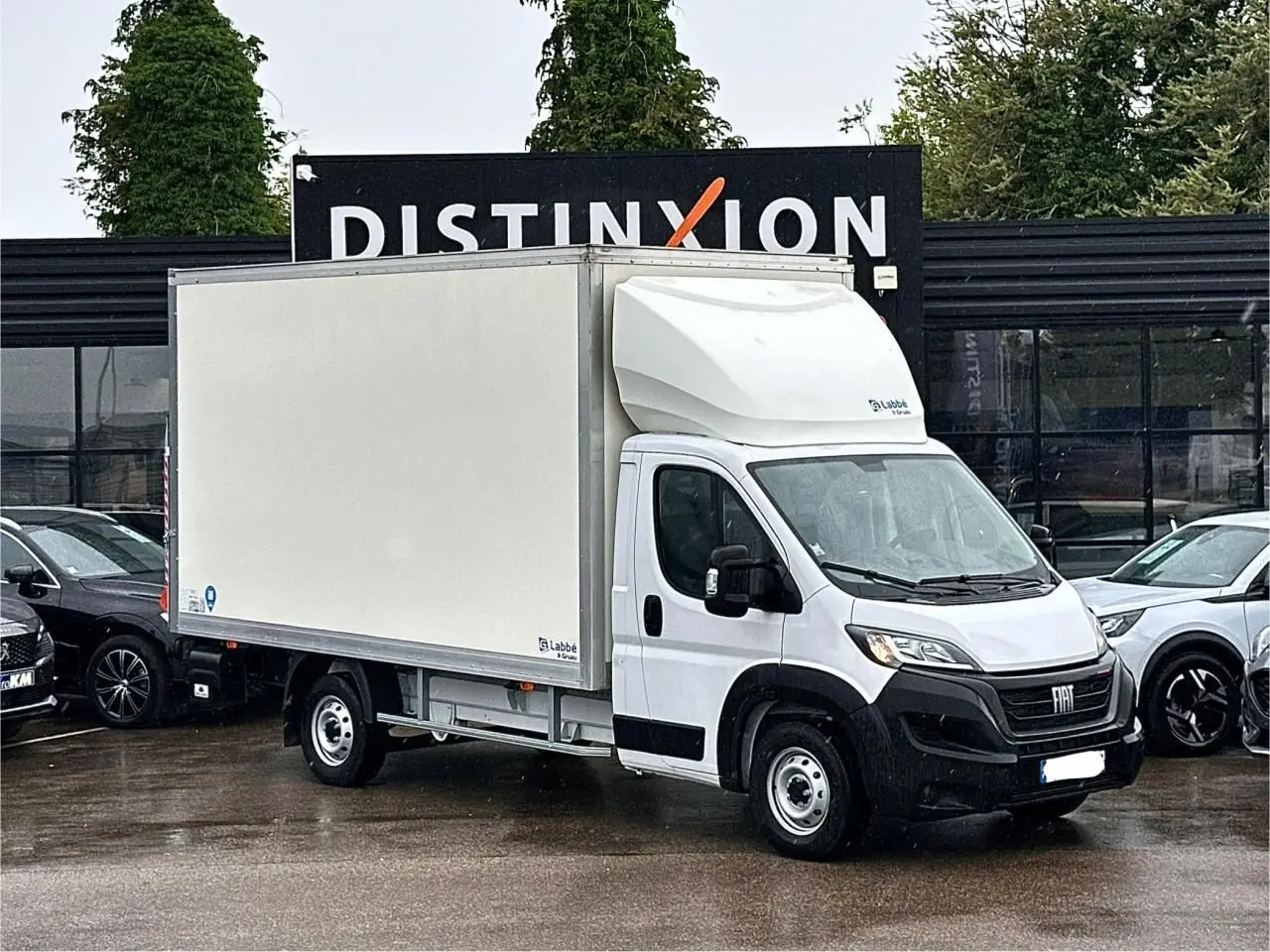 Fiat Ducato Fourgon blanc vu de trois quarts avant droit avec caisse capucine sur parking humide.