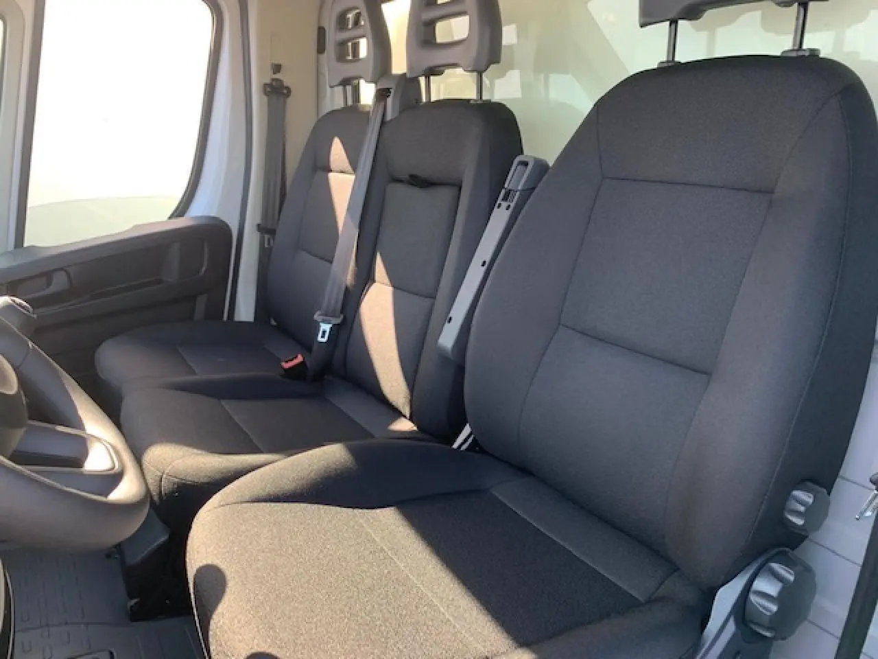 Vue intérieure côté conducteur du Fiat Ducato Fourgon 2022, montrant la banquette passager biplace noire et le siège conducteur noir.