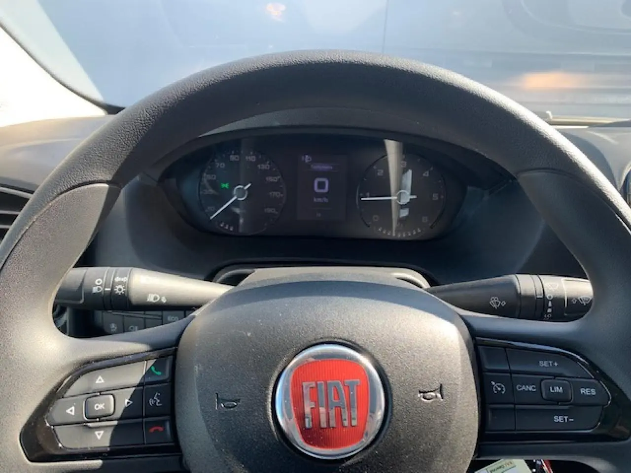 Vue rapprochée du volant noir avec logo rouge FIAT et tableau de bord digital du Fiat Ducato Fourgon blanc 2022.