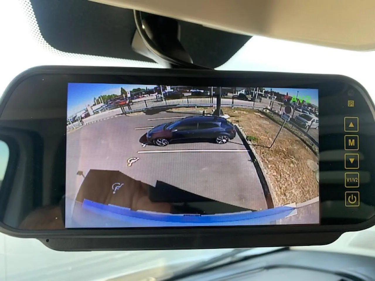 Écran de rétroviseur numérique montrant une vue arrière du parking avec un véhicule noir stationné à droite.