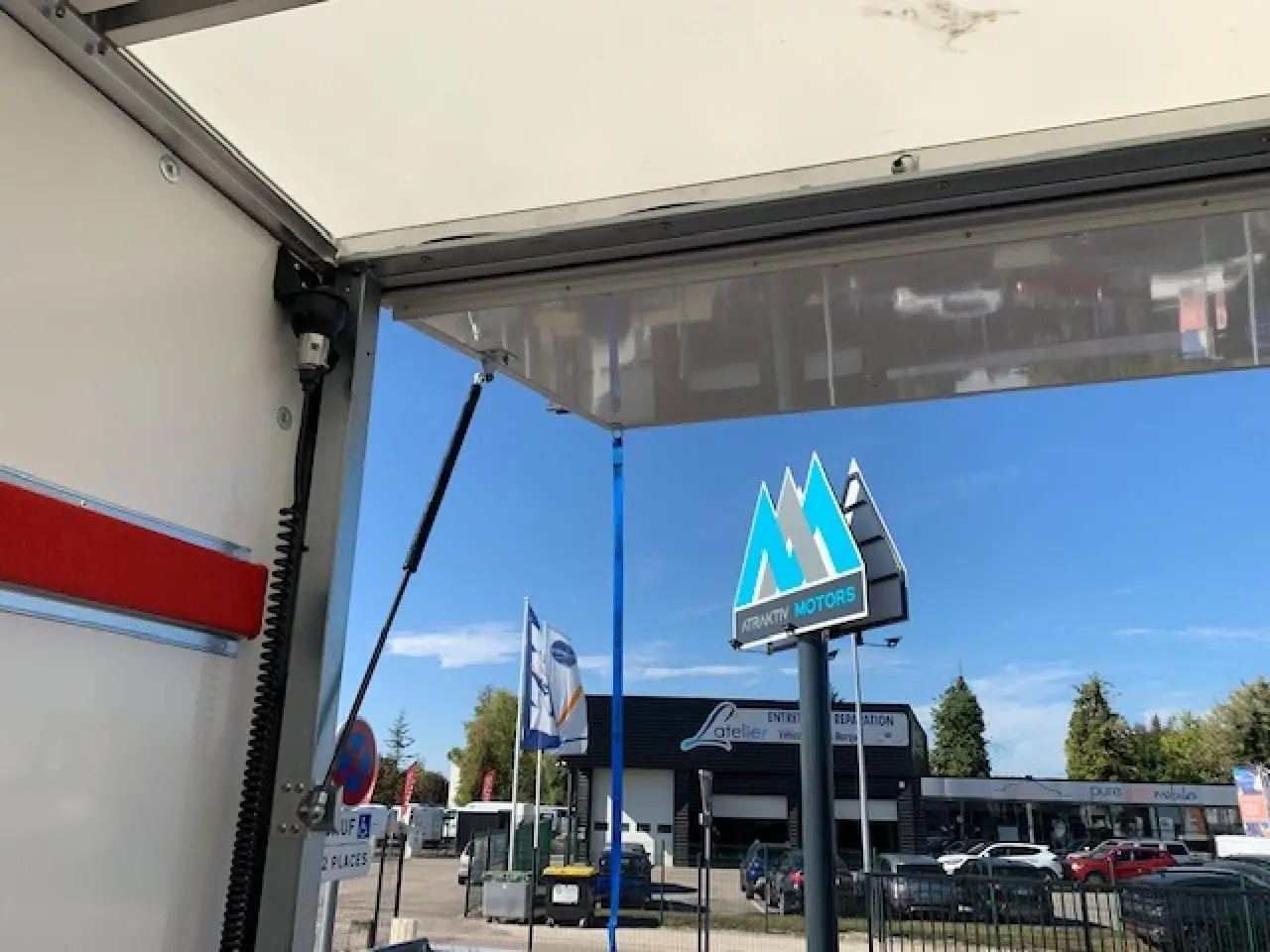 Vue partielle intérieure du hayon ouvert d'un fourgon blanc FIAT Ducato Business, avec ciel bleu et enseigne Attractiv Motors en arrière-plan.