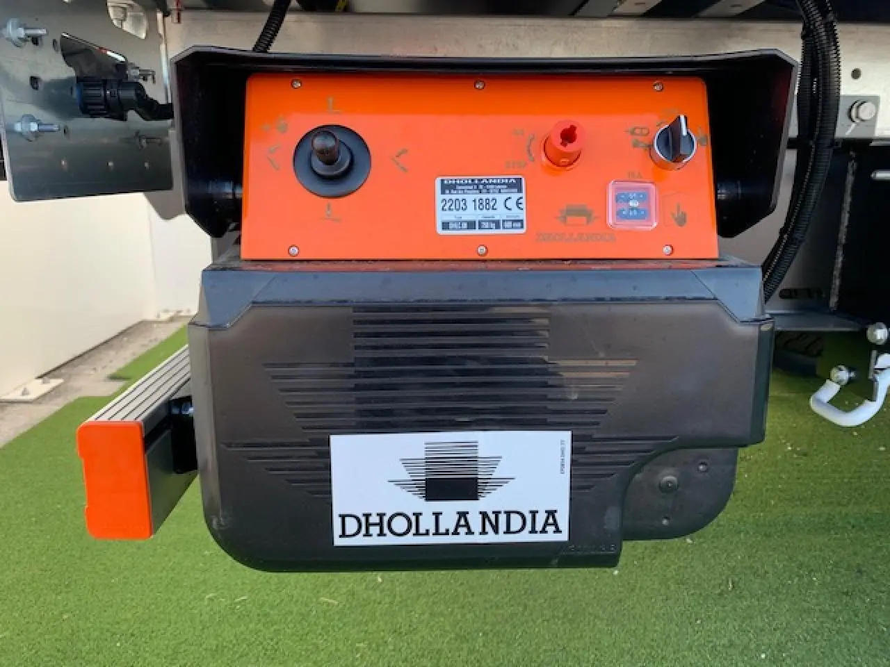 Gros plan sur le mécanisme orange et noir du hayon élévateur Dhollandia fixé à l'arrière du FIAT Ducato blanc.