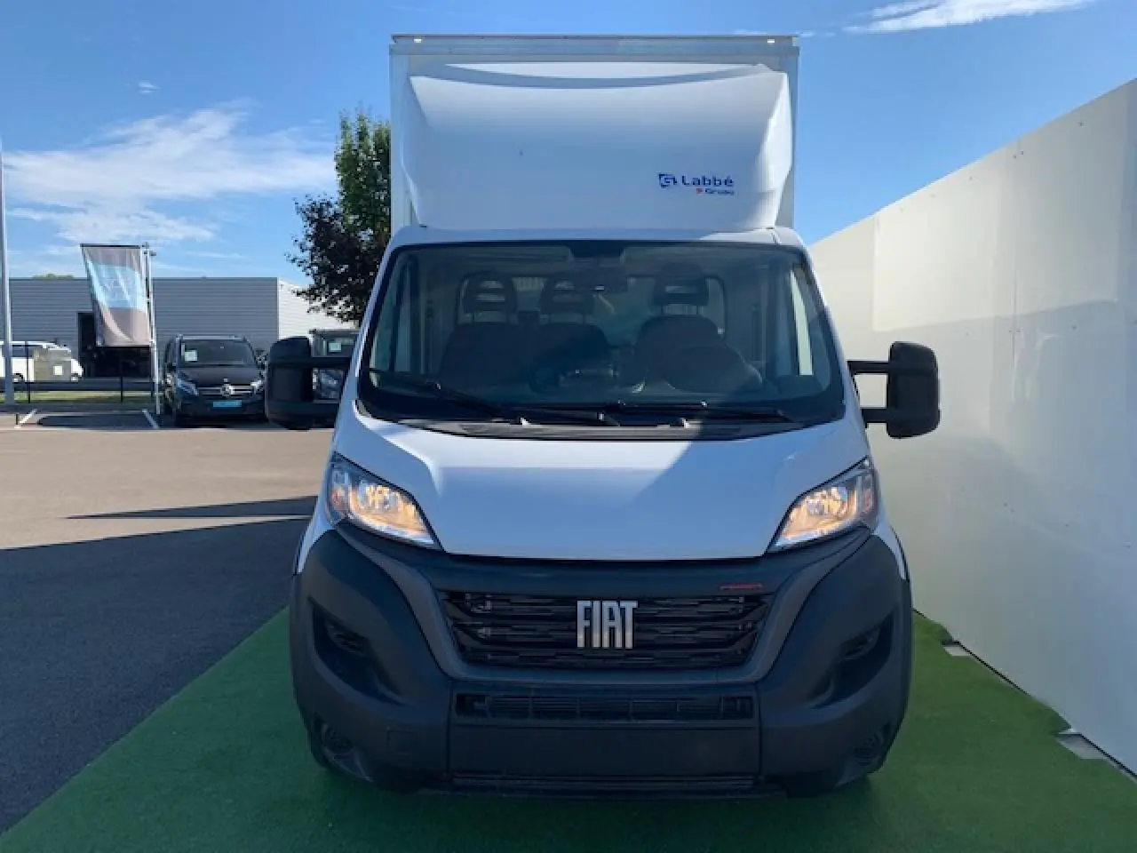 Vue frontale d'un fourgon blanc Fiat Ducato Business 2022 avec hayon et calandre noire visible au soleil.