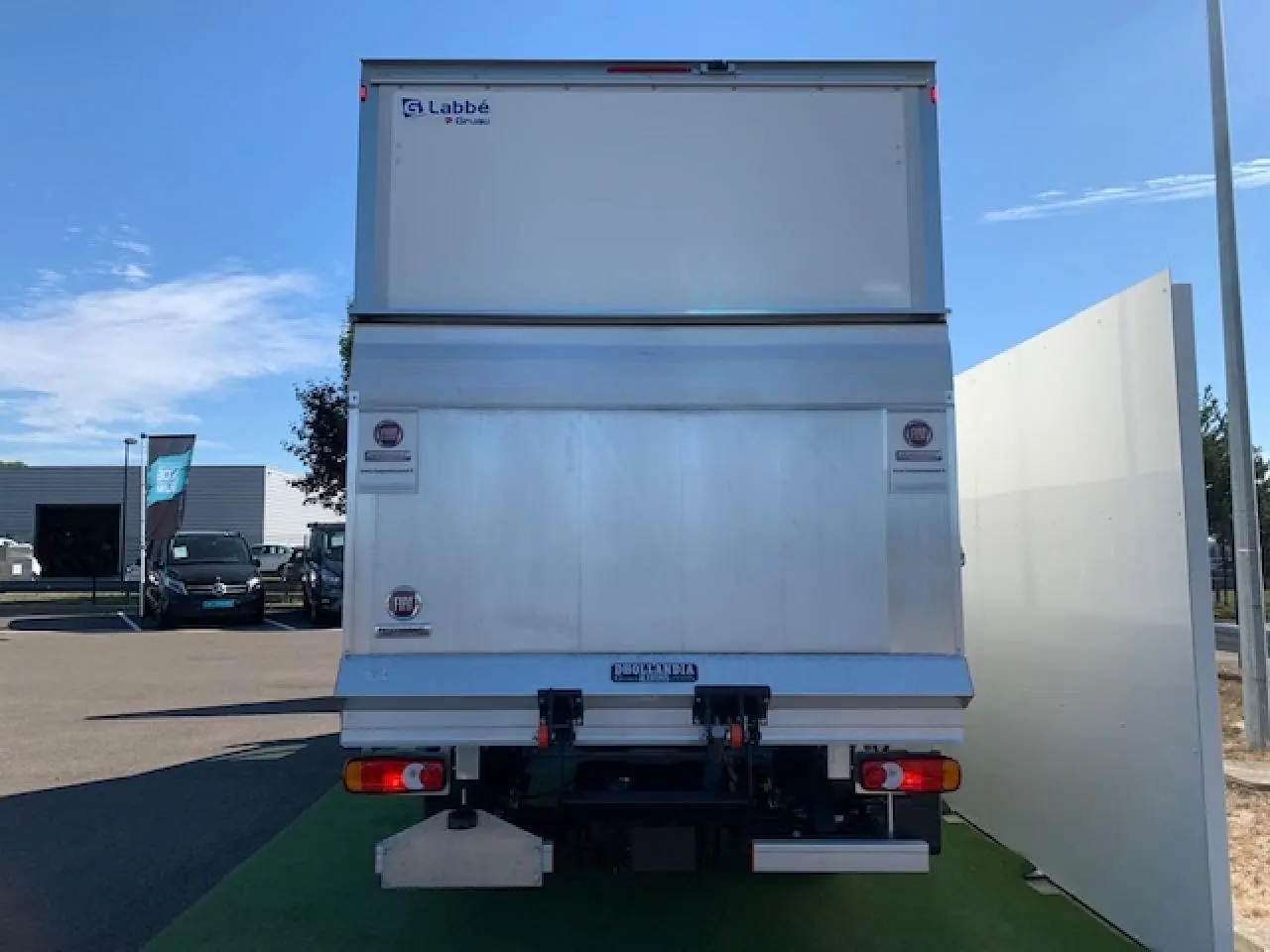 Vue arrière d'un FIAT Ducato Fourgon blanc avec hayon élévateur et marquages Labbé sur un parking.