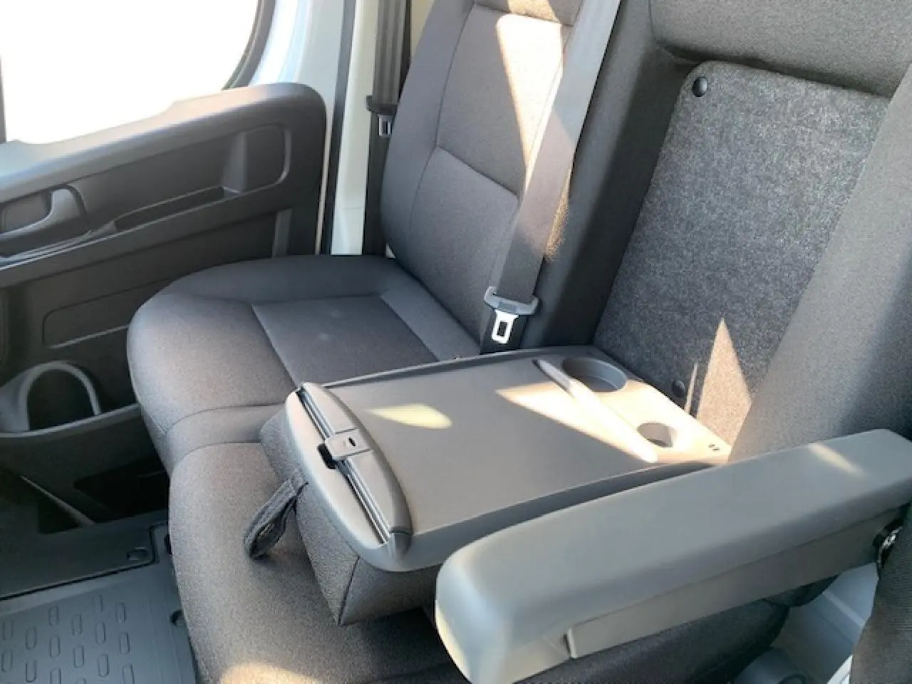 Intérieur du Fiat Ducato Fourgon blanc, vue rapprochée sur la banquette passager biplace avec tablette rabattable et accoudoir.
