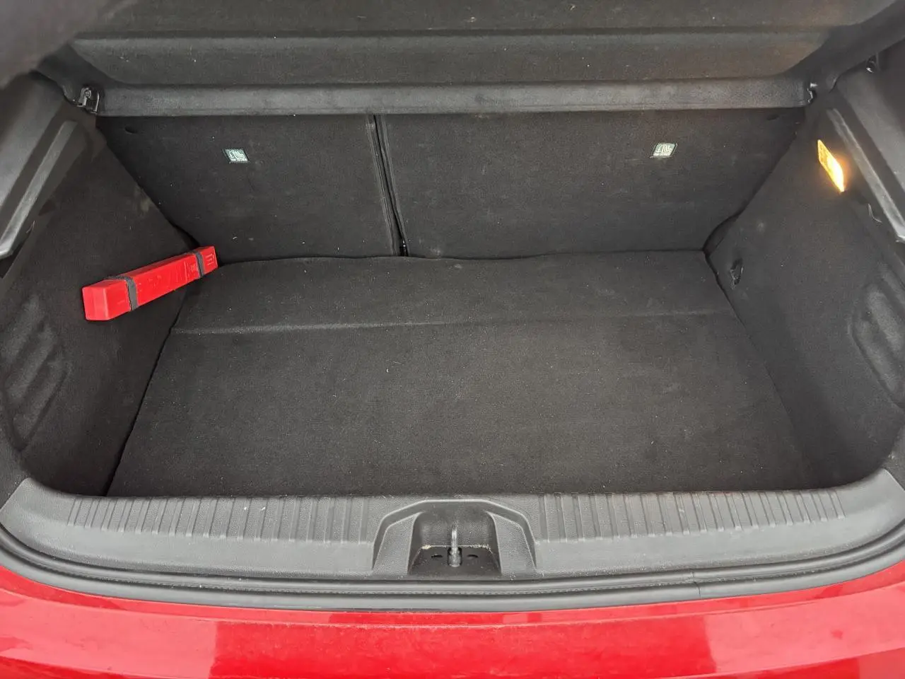Coffre ouvert vu de face d'une Renault Clio rouge flamme, intérieur noir avec triangle de signalisation à gauche.