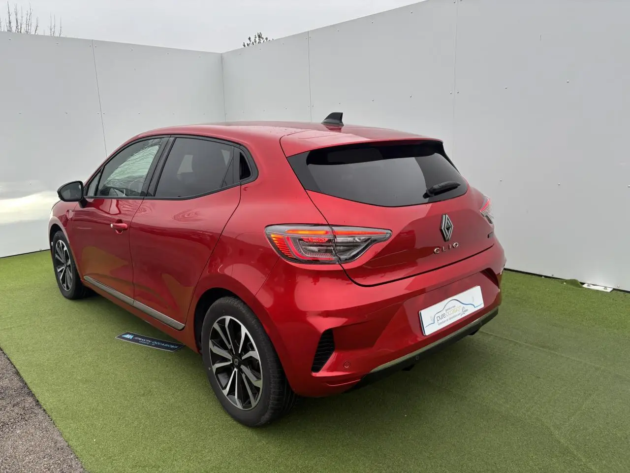 Renault Clio V rouge flamme métal vue 3/4 arrière droit, feux LED et jantes alliage 16 pouces visibles.