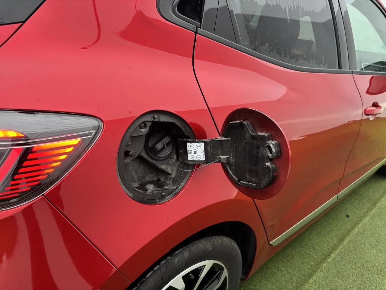 Vue latérale droite de la Renault Clio rouge flamme avec trappe de carburant ouverte et feu arrière allumé.