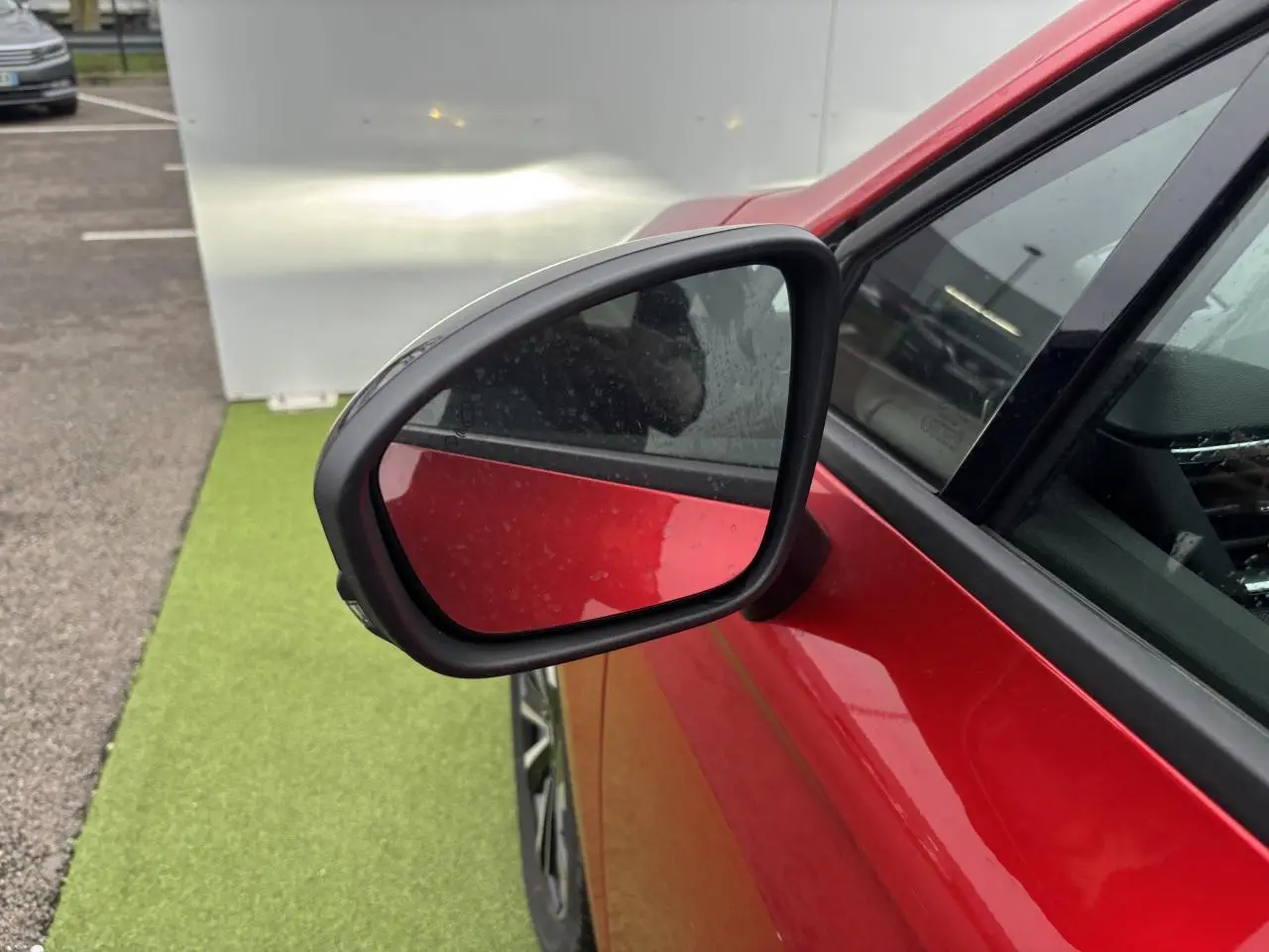 Rétroviseur côté gauche d’une Renault Clio rouge flamme métal, avec partie avant et vitre visible.