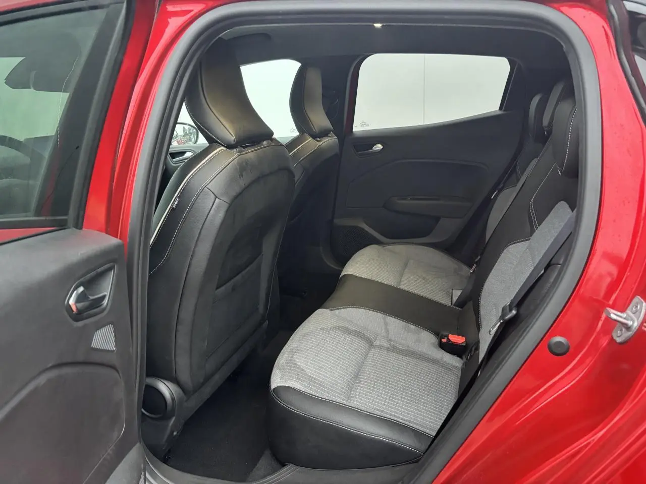 Vue intérieure arrière côté gauche d'une Renault Clio rouge flamme avec sièges arrière gris et noirs.