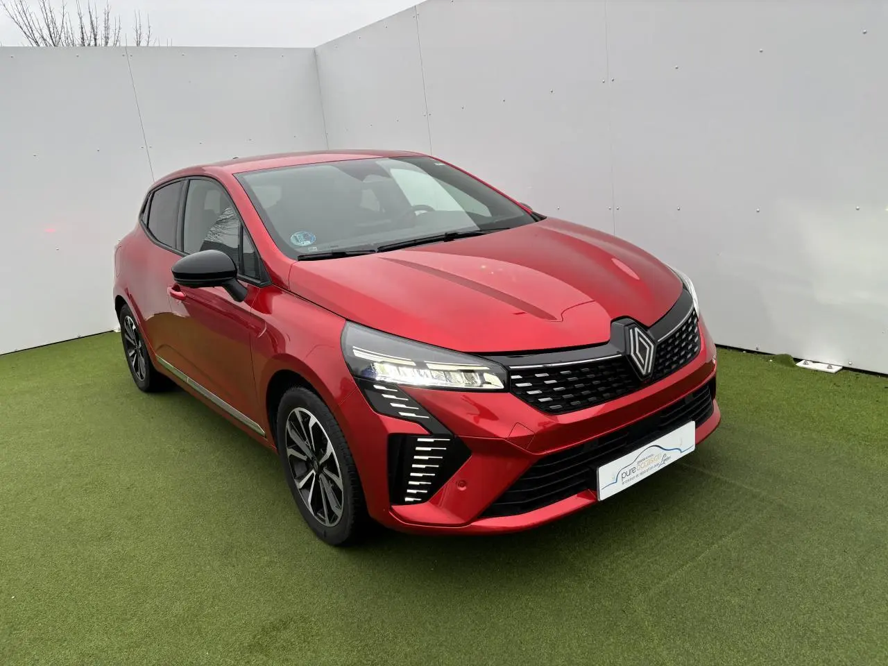 Renault Clio V rouge flamme métal vue 3/4 avant, avec signature lumineuse LED en C et jantes alliage noires.