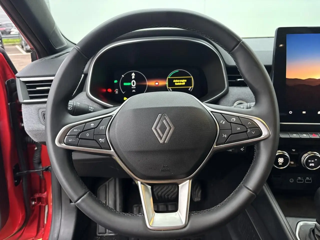 Vue rapprochée du volant multifonction noir et du tableau de bord numérique de la Renault Clio V rouge flamme 2025.