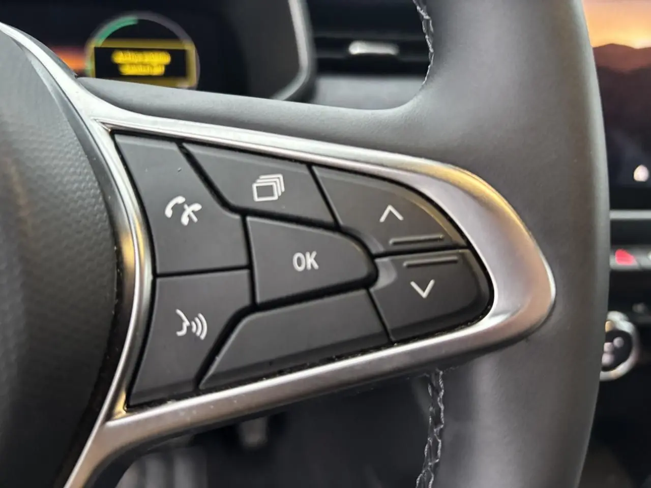 Gros plan sur les commandes multifonctions noires à gauche du volant de la Renault Clio rouge flamme 2025.