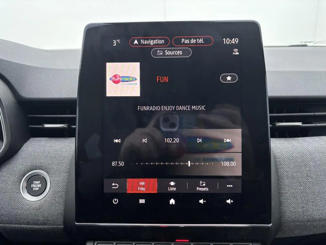 Vue rapprochée de la console centrale de la Renault Clio V rouge flamme, avec écran tactile multimédia allumé affichant la radio.