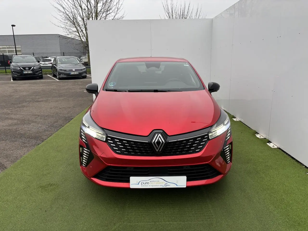 Renault Clio V hybride rouge flamme vue de face, avec calandre noire et feux LED allumés.