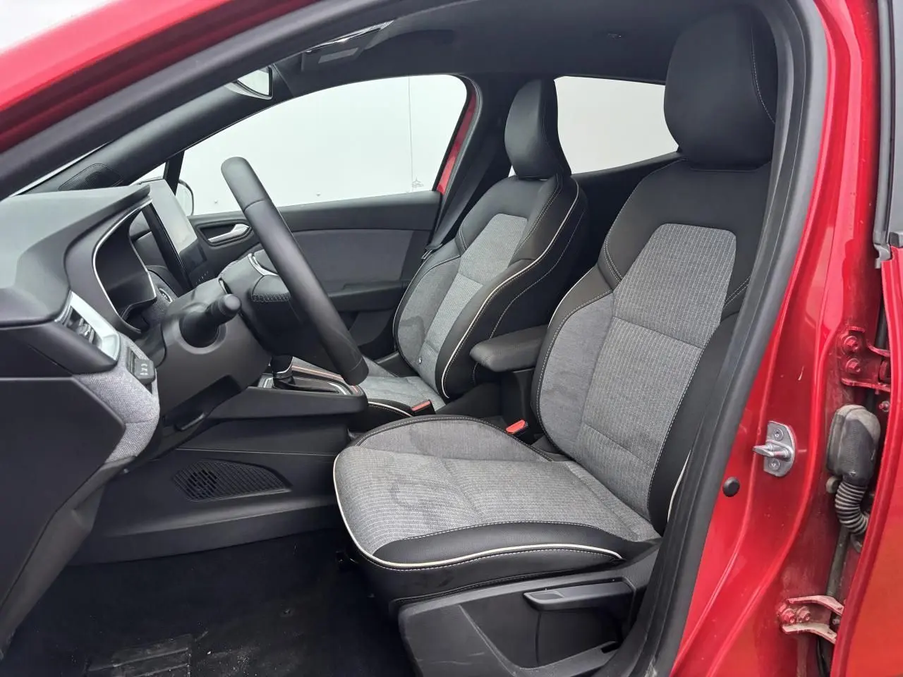 Vue intérieure côté conducteur de la Renault Clio rouge flamme, sièges tissu gris et noir avec surpiqûres claires.