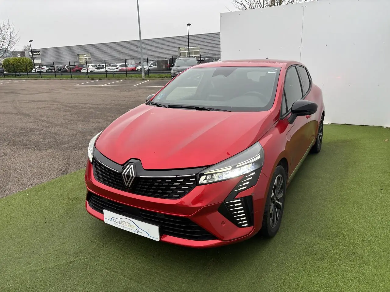Renault Clio V hybride rouge flamme vue 3/4 avant droit, avec signature lumineuse LED distinctive et jantes alliage.