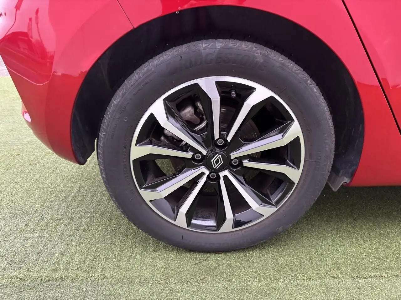 Gros plan sur la roue avant droite avec jante alliage noire et argentée de la Renault Clio rouge flamme.