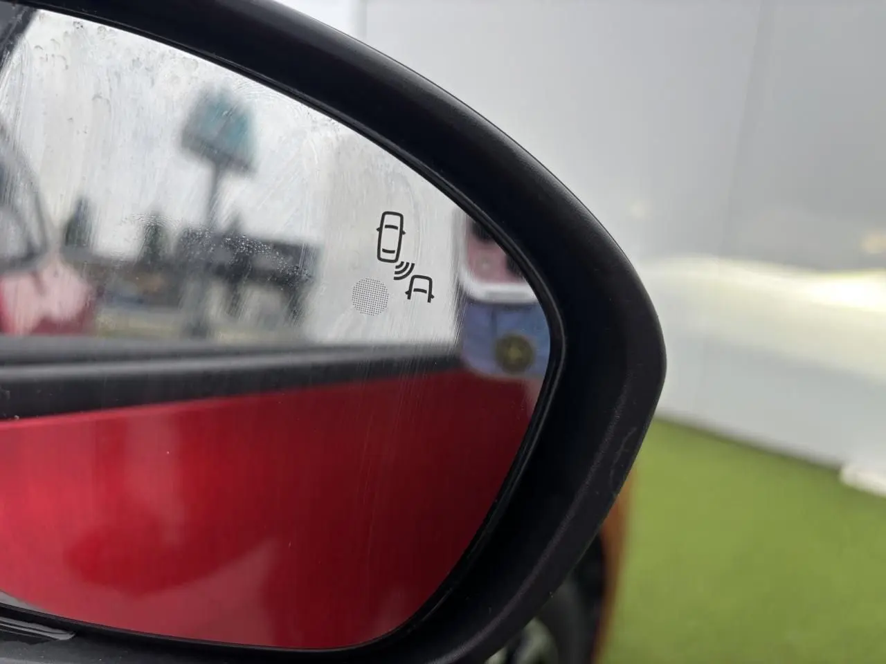 Rétroviseur extérieur côté droit de la Renault Clio rouge flamme, avec indication d'alerte d'angle mort visible.