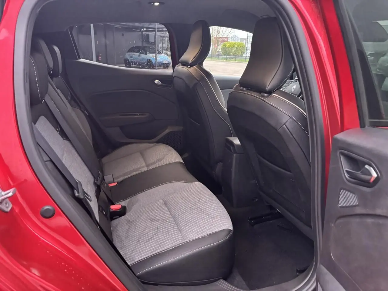 Vue intérieure arrière côté gauche de la Renault Clio V rouge flamme, montrant les sièges tissu et cuir bicolores.