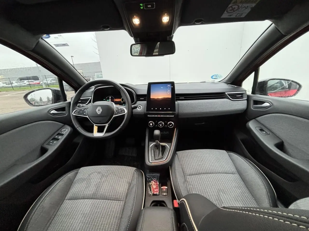 Vue intérieure avant de la Renault Clio V hybride, tableau de bord gris avec écran tactile vertical et volant multifonction.