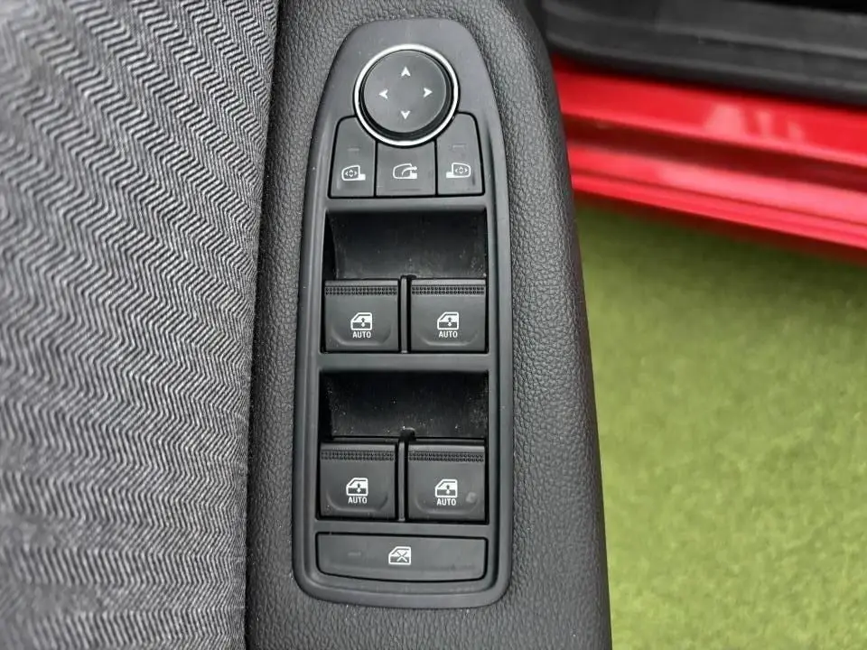 Gros plan sur les commandes des vitres électriques côté gauche avec partie de la porte rouge flamme visible en arrière-plan.