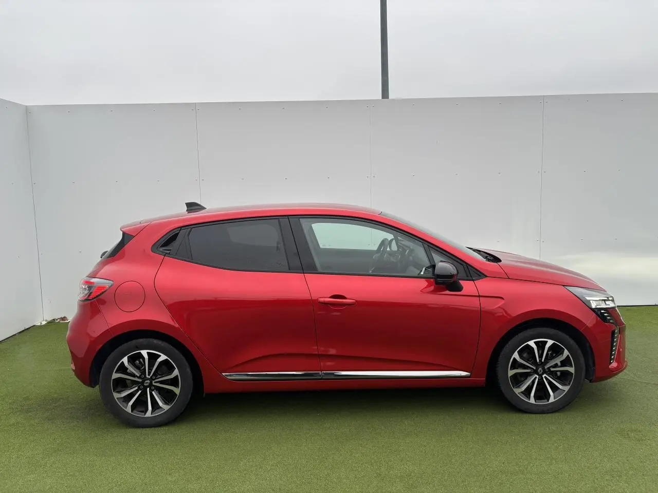 Profil droit d'une Renault Clio 2025 rouge flamme métal avec jantes alliage et vitres surteintées.