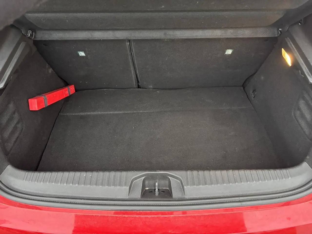 Coffre ouvert de la Renault Clio V rouge flamme, montrant un espace de rangement noir avec un triangle de signalisation.