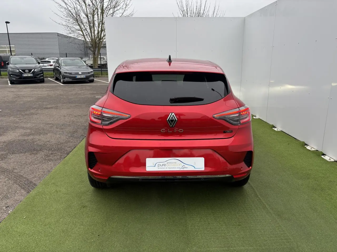 Vue arrière d'une Renault Clio 2025 rouge flamme métal avec feux arrière LED en forme de C et vitre arrière surteintée.