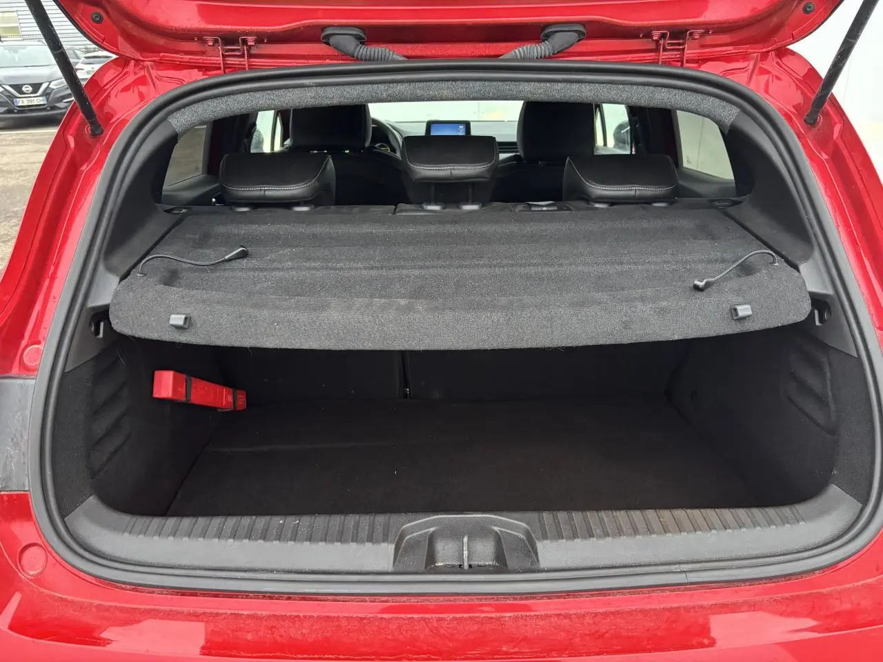 Coffre ouvert vu de l'arrière d'une Renault Clio V rouge flamme, avec cache-bagages en place et sièges arrière visibles.