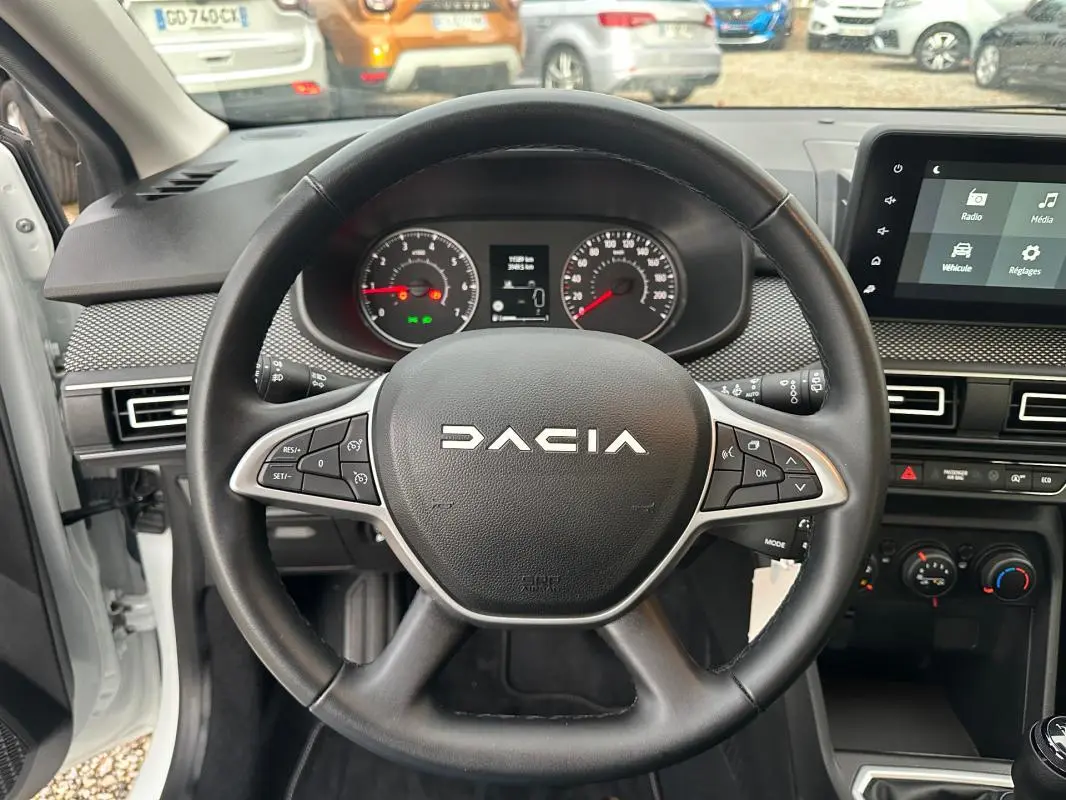 Vue intérieure centrée sur le volant noir de la Dacia Sandero blanche 2024 avec tableau de bord et écran tactile.