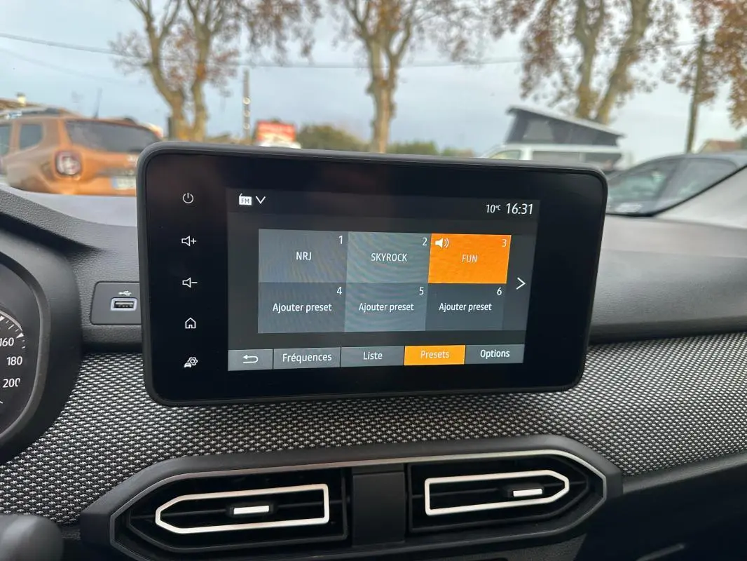 Écran tactile central du tableau de bord de la Dacia Sandero blanc, avec menu radio affiché en extérieur.