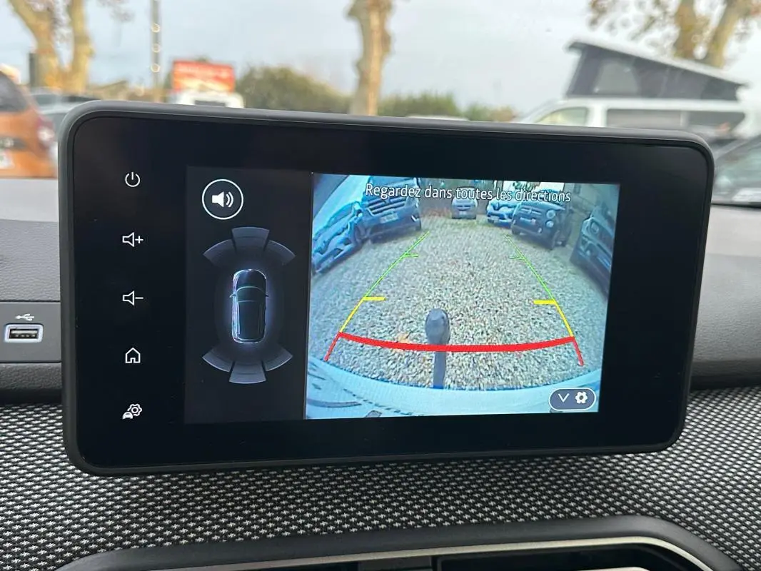 Écran intérieur montrant la caméra de recul active d'une Dacia Sandero blanche, vue depuis le poste de conduite.