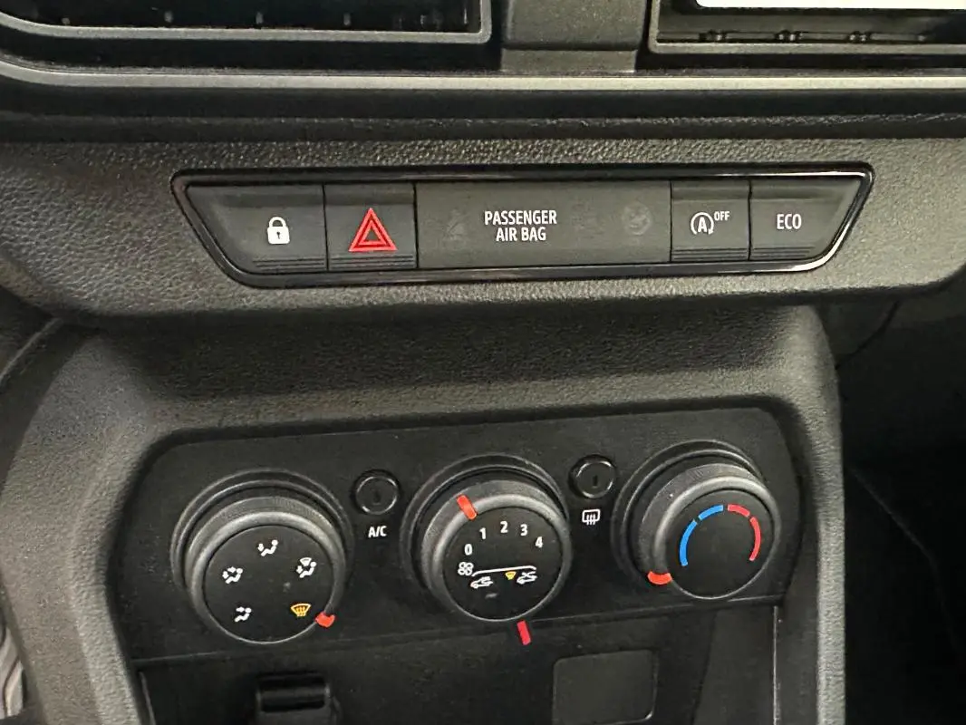 Vue rapprochée du tableau de bord de la Dacia Sandero 2024, montrant les commandes de climatisation manuelle et les boutons de sécurité.