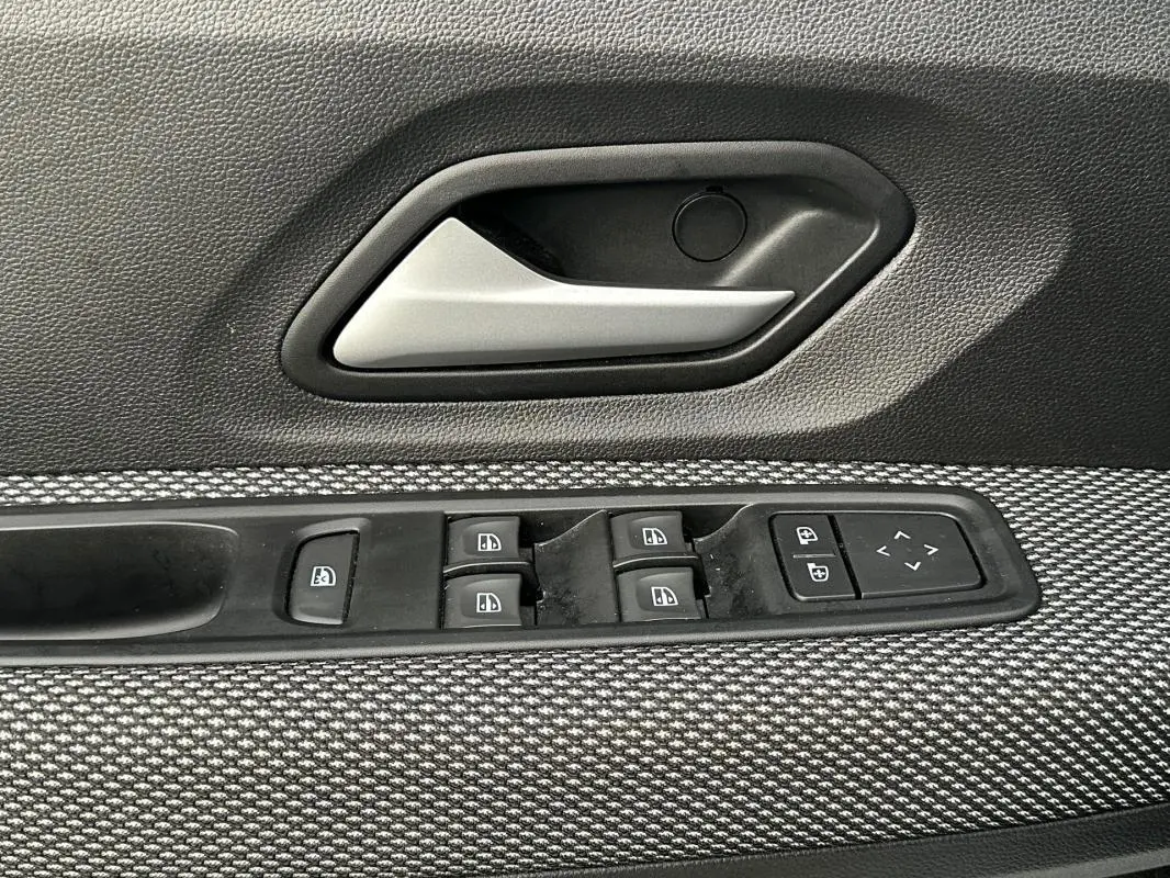 Gros plan sur la poignée intérieure et les commandes des vitres côté gauche d’une Dacia Sandero blanche, tissu gris texturé.