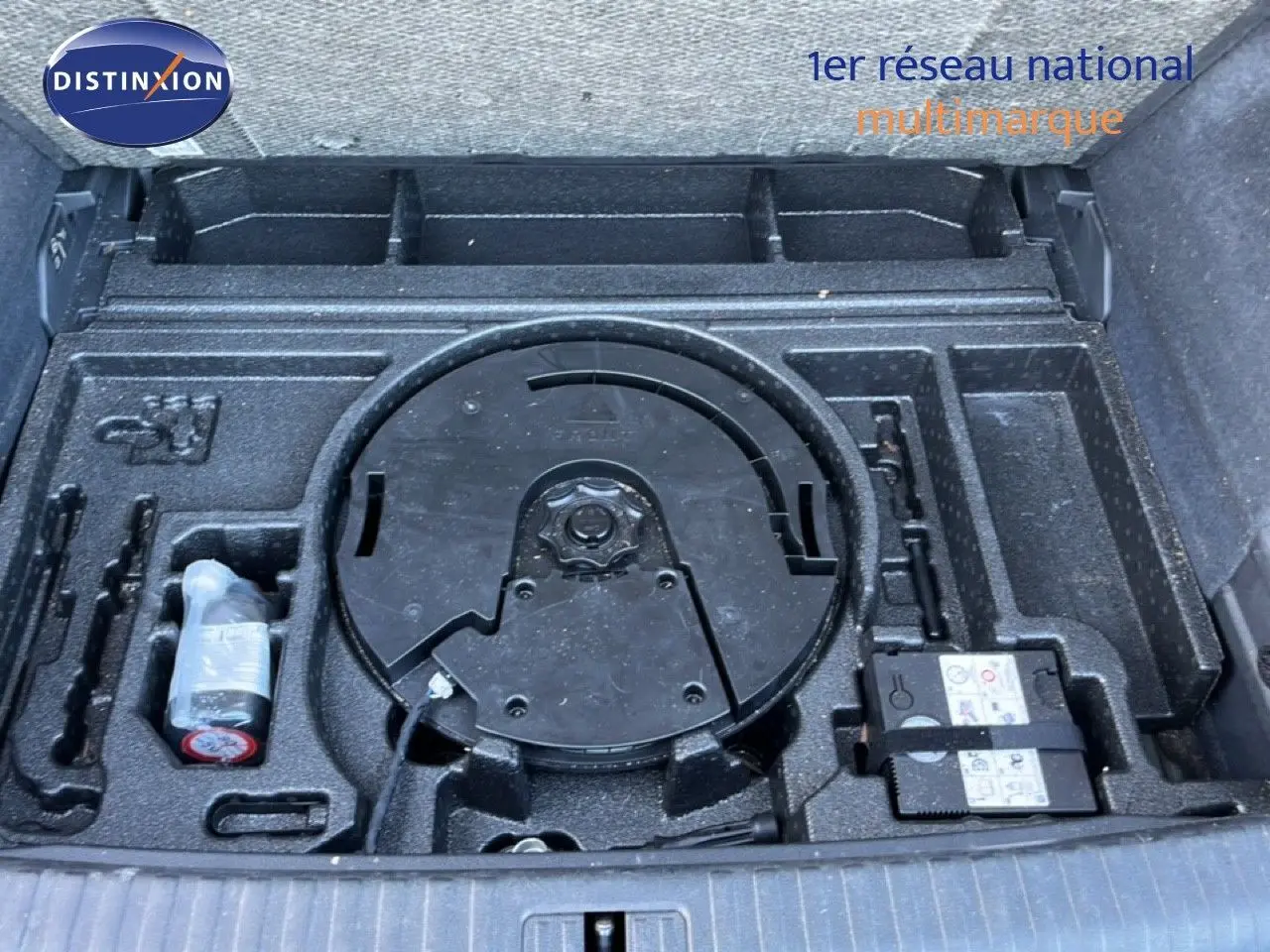 Vue plongeante sur le coffre ouvert d’un Audi Q3 Sportback noir mythic, montrant le rangement pour roue de secours et outils.