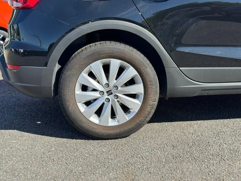 Gros plan sur la roue arrière droite d'une SEAT Arona noire avec jante alu et partie basse de la carrosserie grise.